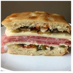 An assemble muffaletta sandwich showing the layers of meat, cheese and olive salad.